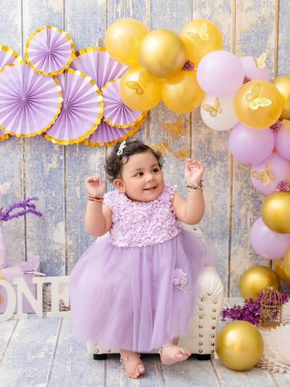 A classic first birthday portrait, with this little one looking absolutely adorable in her lavender dress amidst a matching themed setup.