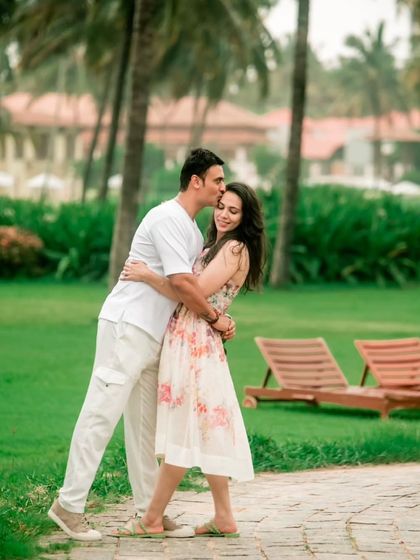 A tender kiss on the forehead, set against the soft-focus background of a lush green resort, creating a classic romantic portrait.