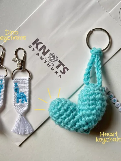 A set of custom keychains, featuring two dino-themed knotted keychains and a personalized crochet heart charm with the name "Jennifer."