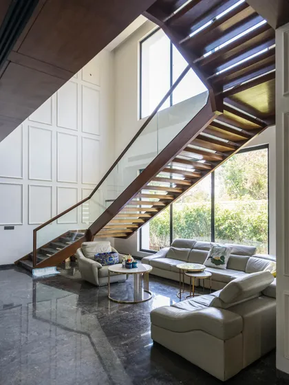 At Triveni Farmhouse, a cozy seating area is nestled under the open, modern staircase. The double-height space is filled with light, and the neoclassical wall mouldings add a touch of timeless elegance.