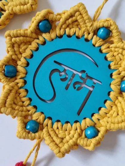 A close-up of the 'Shubh' hanging, showing the Hindi script, the surrounding knot work, and the blue bead details.