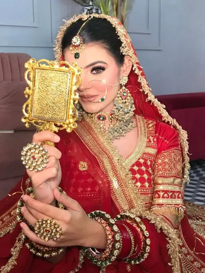 A classic pose with a hand-mirror, reflecting the beauty of this traditional red and gold bridal look.