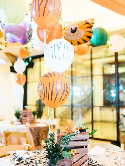 A simple yet effective centerpiece idea for a wild animal theme, using tiger-striped balloons and a rustic wooden crate with foliage.