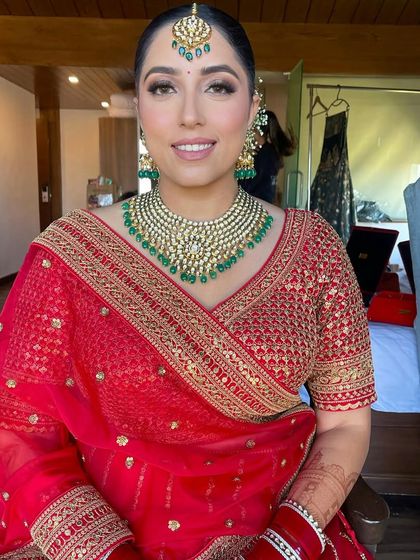 A gorgeous bride in a classic red saree, her hair styled in a neat bun with a floral touch.
