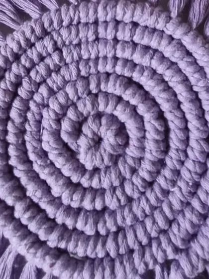 A close-up of a solid lavender spiral coaster, showing the tight knotting and soft fringe.