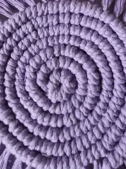 A close-up of a solid lavender spiral coaster, showing the tight knotting and soft fringe.