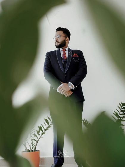 A creative shot of the groom, framed by green leaves, adding an artistic and modern touch to his wedding portraits.