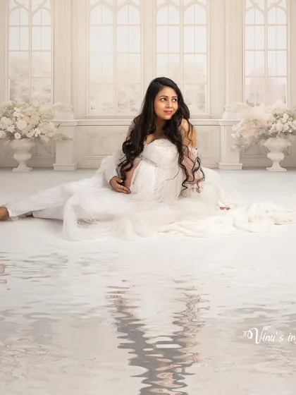 A serene and angelic portrait. The mother-to-be is seated in a heavenly white setting, with the water reflection adding a layer of dream-like calm to the image.