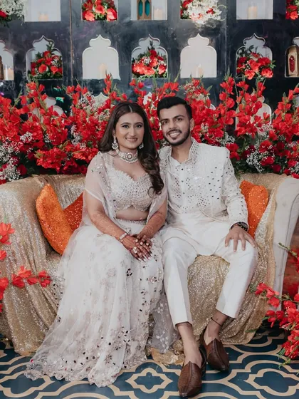 The couple poses against a stunning backdrop of red flowers and gold sequins at their Sufi Night.