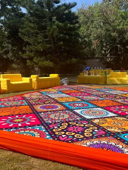 A fun and colorful outdoor Haldi ceremony in progress. I used a vibrant, mandala-patterned floor covering and bright yellow seating to create a joyful and festive environment perfect for the occasion.