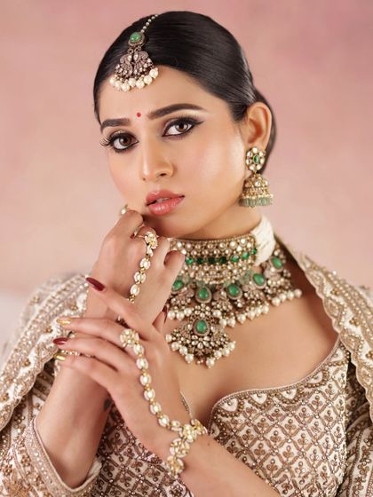 A high-fashion bridal look in an ivory and gold lehenga. The makeup is sharp and defined, with a classic winged liner and a bold brow.