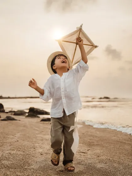 A young boy joyfully runs along the beach at sunset, flying a kite. This image captures the pure, carefree spirit of childhood, perfect for a milestone birthday or a kids outdoor photoshoot.