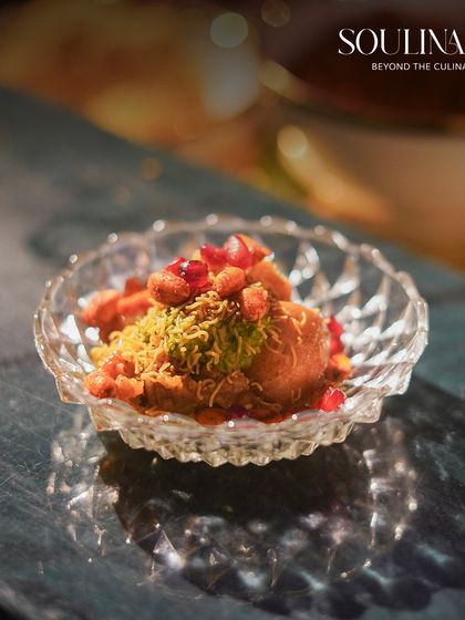 A beautifully crafted bowl of Dahi Bhalla, garnished with pomegranate seeds and savory crisps. This dish represents our modern take on classic Indian wedding fare, served in elegant crystal.