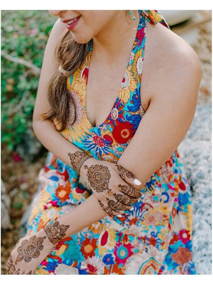 A close-up of the bride's intricate Mehendi design. This shot highlights the artistry of the henna and the vibrant colors of her floral dress.