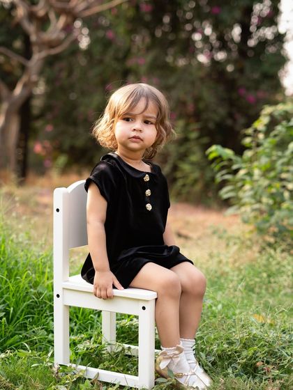 A classic portrait of a toddler sitting on a small chair in a garden. The natural surroundings and soft light create a timeless and beautiful image. These are perfect for framing.