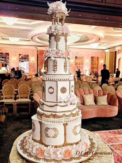 This is the kind of edible masterpiece we love to create. A magnificent, multi-tiered architectural cake designed to be the absolute centerpiece of a grand wedding reception, featuring intricate gold detailing and delicate sugar flowers.