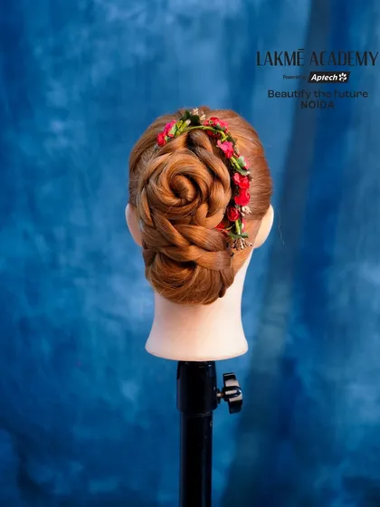 A delicate rose bun created on a mannequin, adorned with a garland of small red flowers.