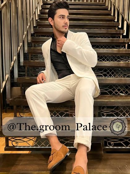 A model relaxes on a staircase in our all-white suit. Paired with a black shirt, this look is a bold and modern choice for a pre-wedding party or a fashion-forward groom.