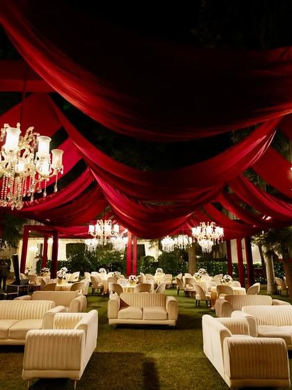 A stunning outdoor reception setup with a ceiling of flowing red fabric and dozens of crystal chandeliers, creating a luxurious and romantic ambiance.