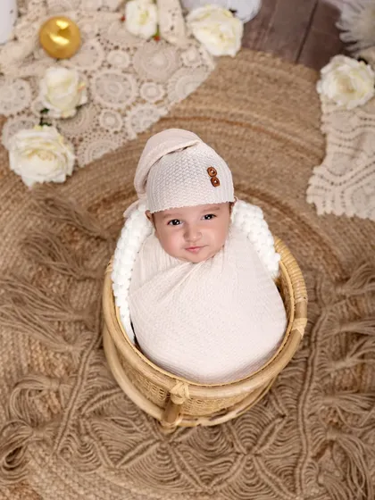 A sweet smile from a swaddled newborn in a wicker basket. The overhead angle and rustic jute rug create a warm and inviting composition.