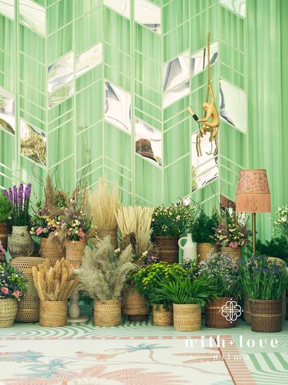 A photo backdrop area from the baby shower, featuring a mirrored wall with a chevron pattern, playful monkey lamps, and an abundance of potted plants and flowers.