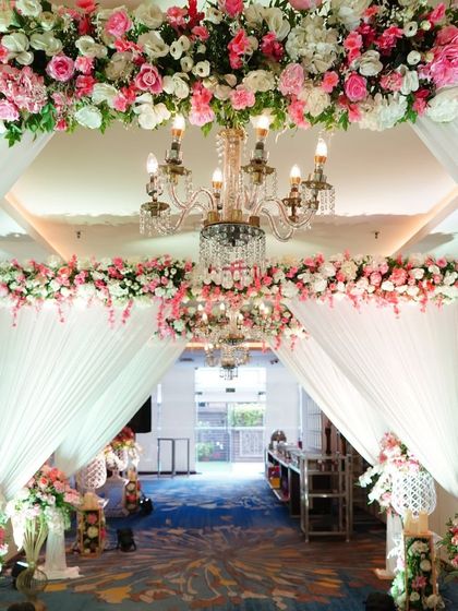 A breathtaking entrance with a ceiling covered in pink and white flowers and multiple crystal chandeliers. The soft white draping adds to the luxurious and dreamy fairytale atmosphere.