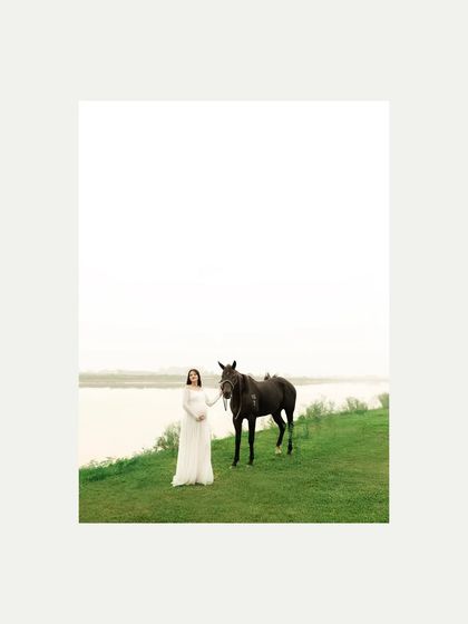 A serene portrait of the mother-to-be with a horse by the water. The foggy, high-key background creates a soft, dreamy atmosphere that is both peaceful and powerful.