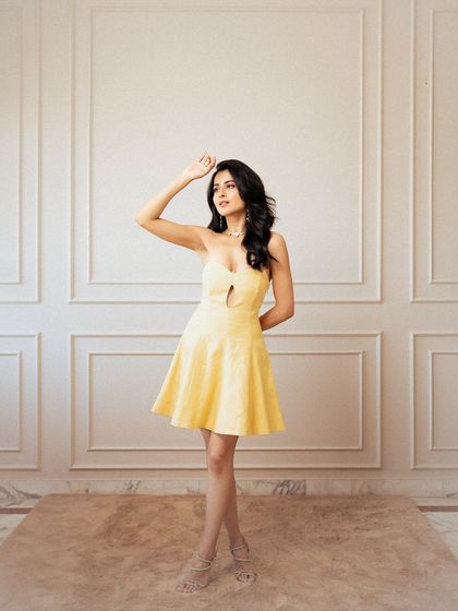 A classic, full-length fashion portrait. The clean background and bright lighting put all the focus on the model and the vibrant yellow dress, creating a timeless and cheerful image.