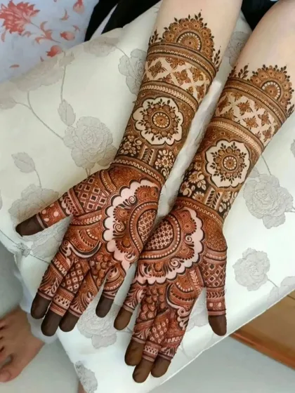 A beautiful, fully covered bridal mehendi with a focus on large mandala patterns on the back of the hands. The arms are adorned with matching geometric and floral bands, creating a cohesive and striking design.