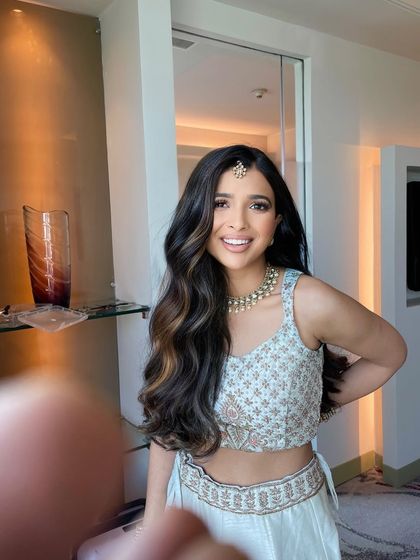 A simple open hairstyle with a center part and soft waves. The look is elevated with a small maang tikka, making it perfect for a pre wedding event.