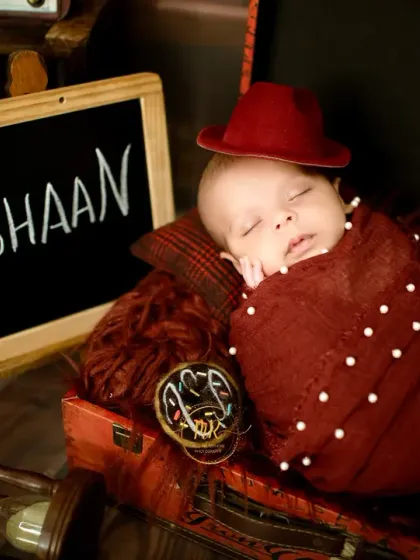 A newborn baby named Tishaan, sleeping soundly in a vintage suitcase setup with a small chalkboard announcing his name.