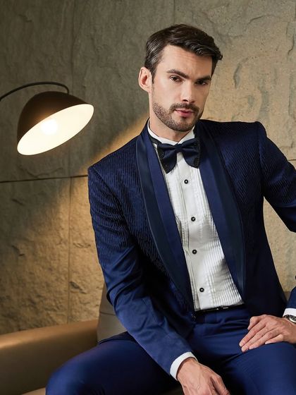 A deep navy blue tuxedo crafted from a textured fabric, offering a rich and distinguished look. The matching navy bow tie and satin lapels create a cohesive and luxurious feel, ideal for any formal occasion.