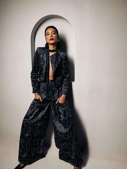 A powerful, full-body shot for the Roologyofficial campaign. The makeup features a strong red lip, and the hair is pulled back to create a clean line, complementing the wide-leg pantsuit.