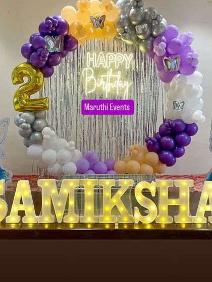 A whimsical fairy-themed party for a 2nd birthday. This setup includes a circular balloon arch, a silver foil curtain, a neon "Happy Birthday" sign, and adorable fairy cutouts.