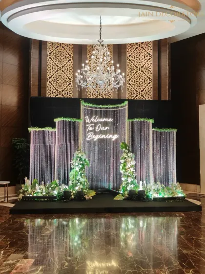 "Welcome To Our Beginning." This photo booth and entrance backdrop features shimmering crystal curtains, a custom neon sign, and lush white florals, setting a glamorous and celebratory tone from the very first moment.