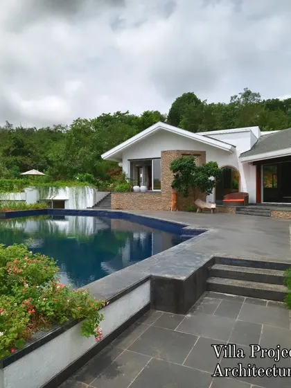 This timeless villa design is surrounded by a landscape that feels both natural and curated. The pool is flanked by stone patios and lush plantings, with a backdrop of dense hillside greenery creating a sense of privacy and seclusion.