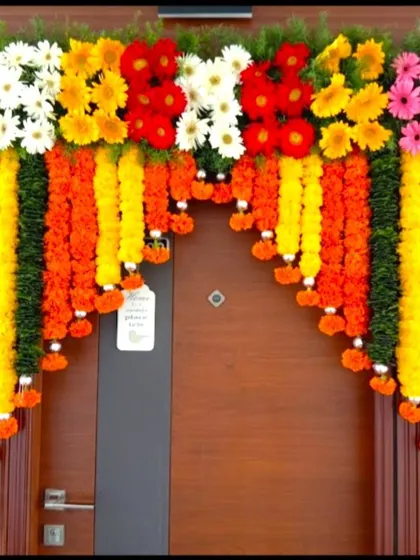 A simple front door flower decoration in Indian style. The door is adorned with hanging garlands of marigolds and a top border of colorful gerberas.
