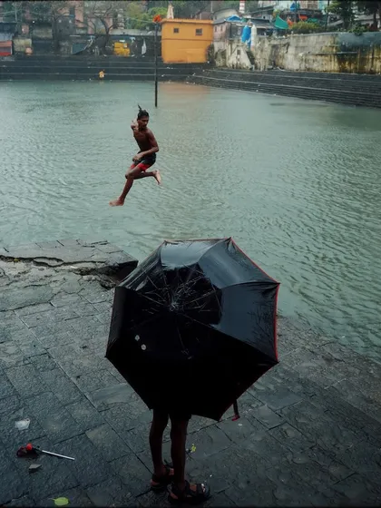 A perfectly timed shot contrasting a still figure under an umbrella with a boy leaping into the water behind. This composition is full of narrative and dynamic tension.