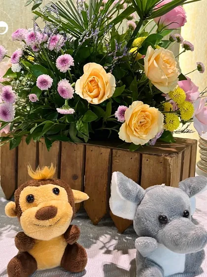 Cute monkey and elephant plush toys sit in front of a rustic wooden crate filled with flowers. These playful details were a hit at the barnyard themed baby shower.