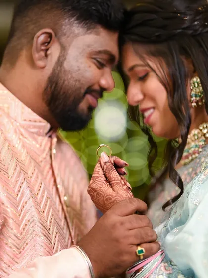 A close-up portrait that puts the engagement ring in focus. The bride's henna-adorned hand gently holds the ring, symbolizing the start of their forever, with a beautiful bokeh light background.
