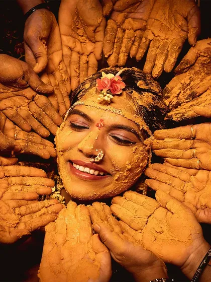 The pure joy of a Haldi ceremony. This photo captures the bride's beautiful smile as her loved ones surround her, their hands covered in turmeric, blessing her before her big day. It's a moment of tradition, love, and happiness.