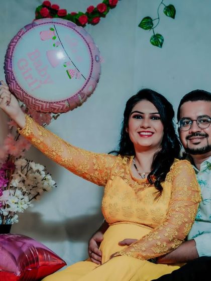 A fun studio shot celebrating an upcoming baby shower or gender reveal. The couple holds balloons while sharing a happy moment, showcasing a more playful side of their maternity journey.