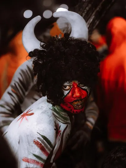An intense close-up of a performer with striking red and white face paint and horns. The dramatic lighting and tight crop highlight the incredible artistry and character of the costume.