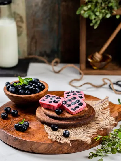 For these blueberry chocolates, I created a fresh and appealing scene with a bowl of fresh blueberries on a wooden board. The composition feels wholesome and delicious, highlighting the natural fruit ingredients.