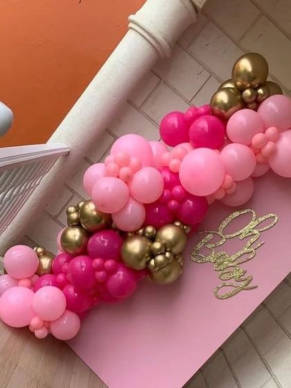 A close-up of a heart-shaped "Oh Baby" sign with a vibrant pink and gold mini balloon garland, perfect as a cake topper or decor accent.