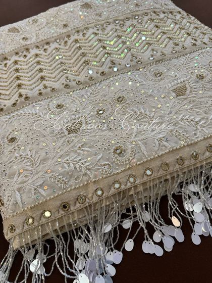 A detail shot of the saree's border and pallu, showing the intricate combination of Chikankari, mirrorwork, and shimmering sequins, complete with delicate tassels.