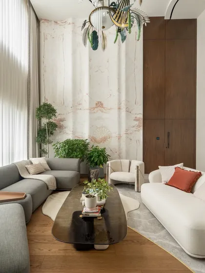 A closer look at the seating arrangement in the Kolkata living room. We used a mix of curved sofas in white and grey to soften the space, centered around a smoked glass coffee table. The handcrafted marble wall serves as a stunning backdrop.