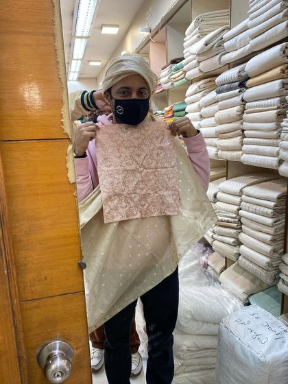 A behind-the-scenes shot of the safa selection process. Holding up the fabric swatch for the sherwani against the safa cloth ensures a perfect color and texture match.