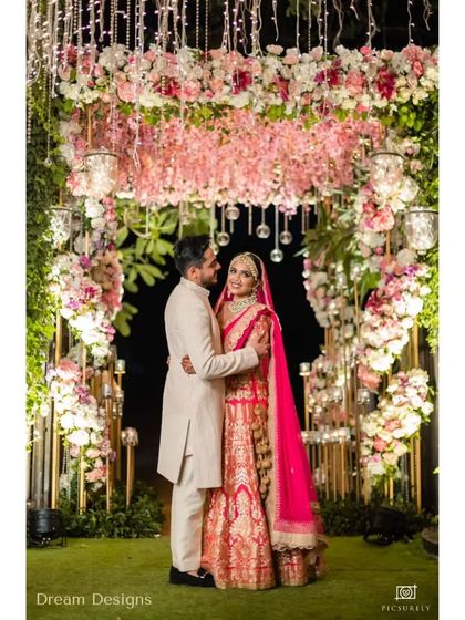 A beautiful couple portrait taken under a romantic floral arch. The arch is filled with pink and white flowers, with hanging glass globes and candles adding a magical glow.