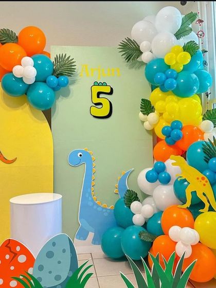 The main backdrop for Arjun's 5th birthday, featuring a friendly blue dinosaur and a vibrant balloon arrangement.